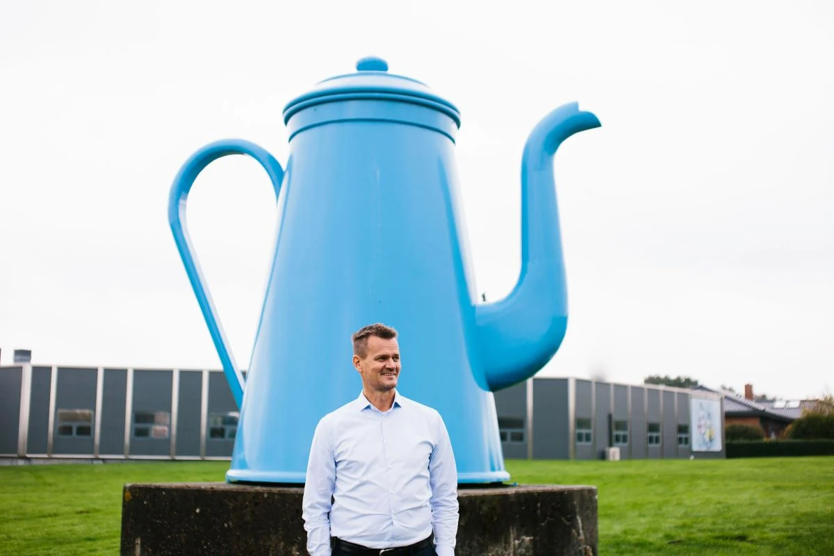Direktør hos Peter Larsen Kaffe, Claus Bertelsen erkender at kaffepriserne vil stige. Her portrætteret foran kaffeproducentens hovedkontor i selskab af den ikoniske kaffekande Madam Blå. (Foto: Peter Larsen Kaffe)