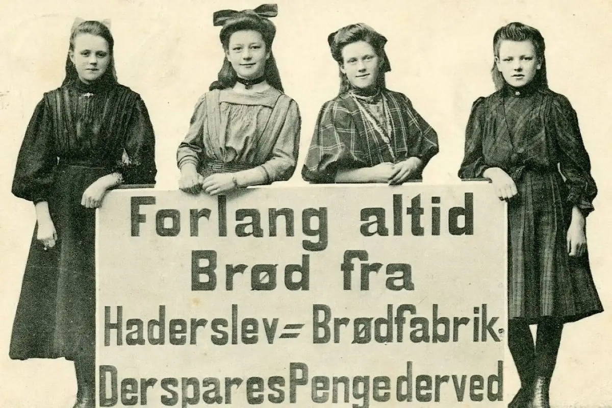 <b>Sønderjylland 1910: Hold styr på pengene - gå til bageren!</b> Fire unge piger poserer og gør reklame med et skilt med påteksten: Forlang altid Brød fra Haderslev Brødfabrik. Der spares Penge derved. Haderslev Brødfabrik, dengang Erlevvej 28 - i dag ligger den på Odinsvej 2. Spis lige brød til, siger vi fra Oldmoney! (Foto: Historisk Arkiv for Haderslev Kommune)