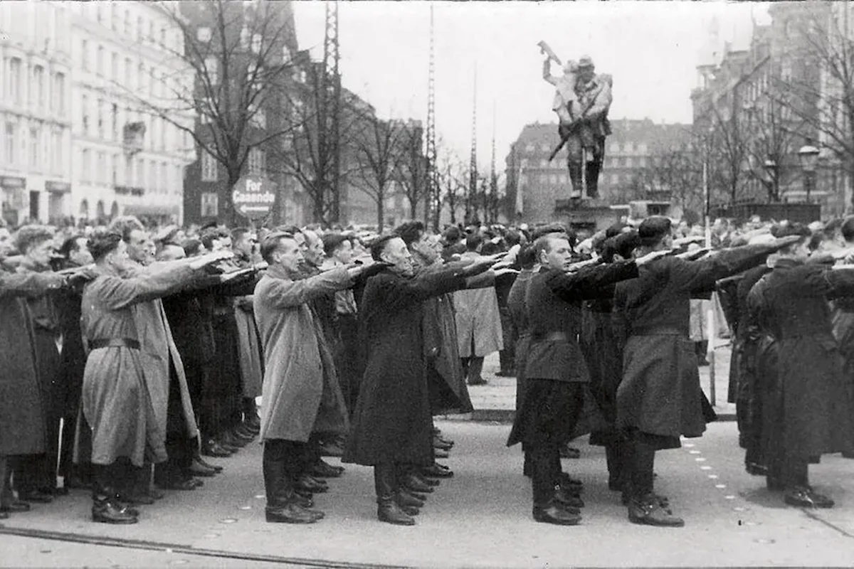 <b>København 1940: Danmark besættes.</b> Den 17. november 1940 samledes det danske nazistparti, DNSAP, foran statuen Den Lille Hornblæser i håb om at komme til magten. Overfor ligger Dagmarhus, der ligner sig selv i dag – bortset fra luftværnsbatterierne, der fyldte på bygningens tag under besættelsen. (Foto: fra bogen <i>Turen går til besættelsestidens København</i>)