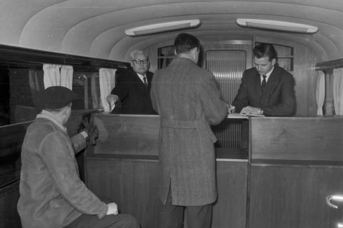 <b>Midtjylland 1964: Ny bankbus.</b> Den nye bus fra Folkebanken for Herning og Omegn kørte rundt til de små landsbyer i det midtjyske bl.a. Arnborg, Fjelstervang, Haunstrup, Høgild, Kølkær, Rimmerhus, Sinding, Skibbild, Studsgaard, Tanderupkjær, Timring, Vorgod og Ørre. Bankbussen holdt også ved en enkel pensionist, som ikke var i stand til at bevæge sig til bankbussen, når hun skulle have udbetalt sin pension. Bankbussen gjorde ophold i de større landsbyer 1 time og i de mindre ½ time. Nogle landsbyer fik besøg 2 gange om ugen, andre kun en enkelt. I nogle af landsbyerne havde banken et telefonstik, hvor man tilsluttede bankbussens telefon. Kunderne var bl.a pensionister, som skulle hæve eller indsætte penge på deres bankbøger, børn som skulle have tømt deres Rasmus Klump-sparebøsse og sat pengene ind på en opsparingskonto, og erhvervsdrivende (købmænd, landmænd, bagere og andre) som indsatte penge på deres kassekredit.
Veksler blev omsat. I de landsbyer, hvor der stod en telefonboks, tømte personalet telefonboksen for penge. Herefter talte de mønterne og indsatte beløbet på Jydsk Telefons konto i banken. Personalet var en chauffør, som var bankuddannet og bankelev. Frokostpausen blev holdt i lokalet bagerst i bussen. - Kom der kunder, afbryd vi frokostpausen, fortæller en pensionær. (Foto: Lokalhistorisk Arkiv i Herning)