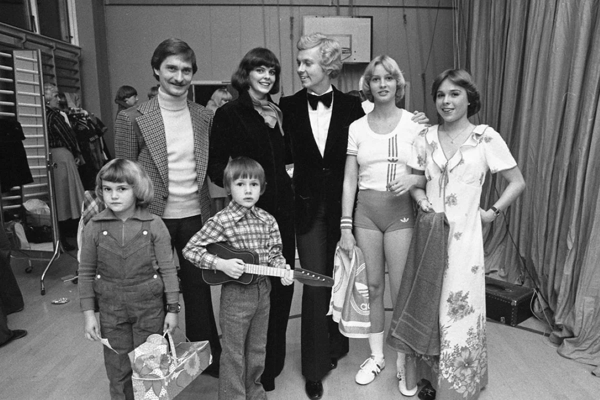 <b>Vejle 1976: Modeshow og bingo med Henrik Krogsgaard.</b> Kombinationen af bingo, modeopvisning og show var noget af et tilløbsstykke i Vejle. I hvert fald var der 400-500 mennesker til Dansk Arbejdes store arrangement i Petersmindehallen. Her aftenens konferencier Henrik Krogsgaard omgivet af mannequiner og dressmen, der viste ny mode fra en række Vejle-butikker for at øge deres salg. (Foto: Vejle Stadsarkiv)