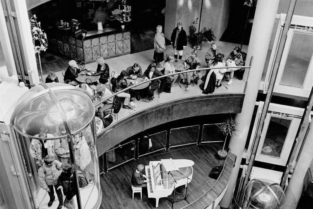 <b>København 1989: Velkommen i det moderne stormagasin.</b> Det er året for murens fald og Sovjetunionens sammenbrud, men i Københavns handelsliv hersker der økonomisk fremgang og velstand blomstrer blandt de forbrugende københavnersnuder. Her billede fra det nyåbnede indkøbscenter Scala på Vesterbrogade i København, der efter en årelang ombygning kunne slå dørene op for butikker, restauranter, fitnesscenter, biograf og tilmed et diskotek i kælderen med plads til 1.000 mennesker. Kapelmesteren ved det hvide flyglet ud til centrets hall, muligvis Henrik Krogsgaard, spiller op til dansant. (Foto: Københavns Museum)